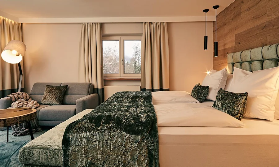 Modernes Zimmer mit Doppelbett, Sofa, Holztisch und großen Fenstern mit Vorhängen