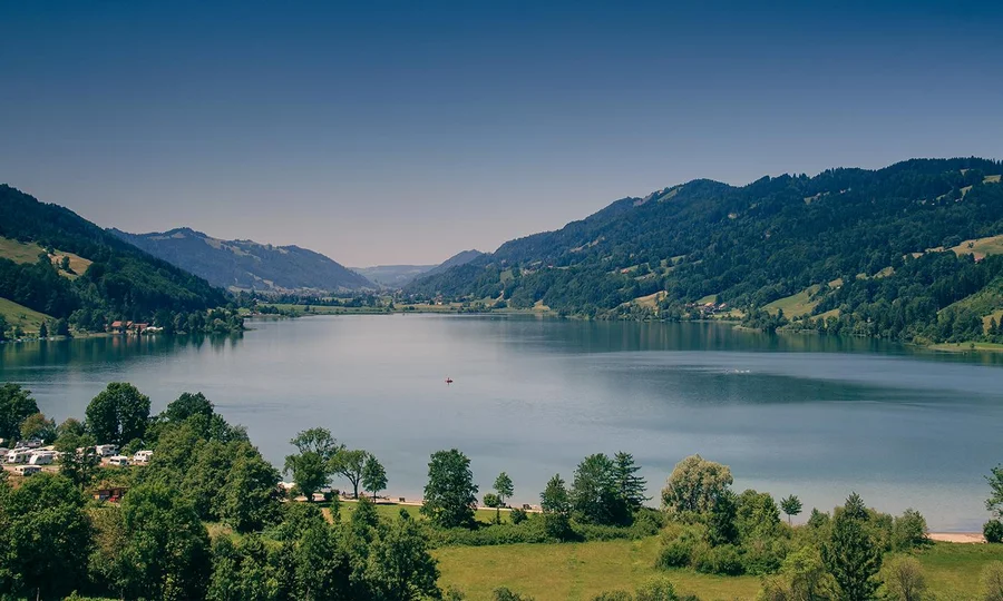 Panoramaaufnahme des Großen Alpsees mit grünen Hügeln und Bergen.