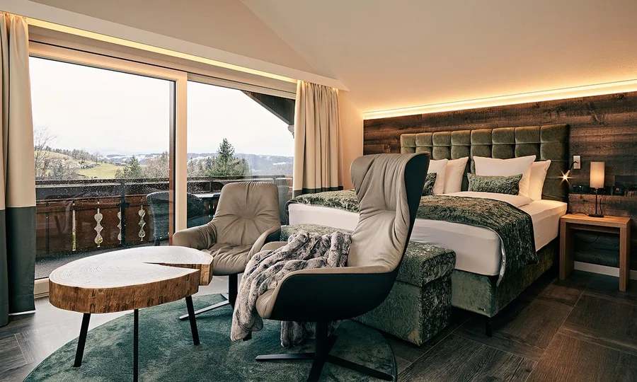 Großzügiges Zimmer mit Doppelbett, Sesseln, Couchtisch und Panoramablick durch große Fenster