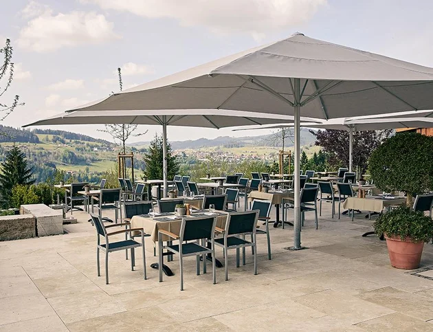 Terrasse mit Sonnenschirmen und mehreren Tischen, Blick auf die Landschaft.
