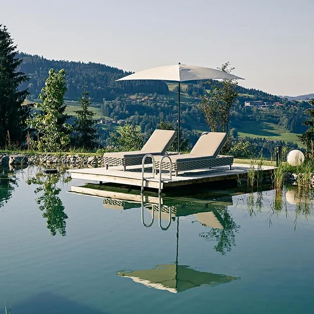 Zwei Liegen am Naturschwimmteich mit Sonnenschirm im Sommer