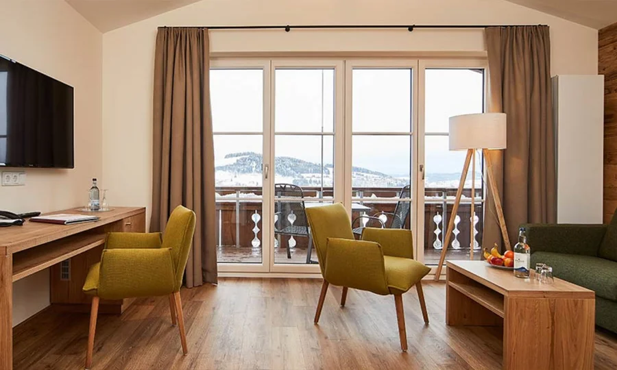 Helles Wohnzimmer mit zwei grünen Sesseln, großem Fenster und Blick auf die verschneiten Berge