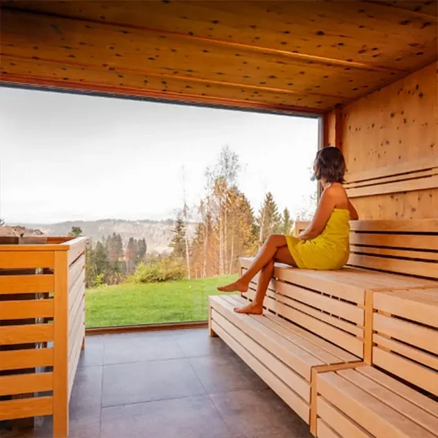 Frau entspannt in der Panoramasauna mit Ausblick auf die Allgäuer Landschaft im Hotel Birkenhof Oberstaufen.