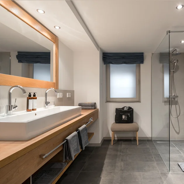 Modernes Badezimmer mit Doppelwaschbecken, großer Spiegelwand und ebenerdiger Dusche im Hotel Birkenhof in Oberstaufen.