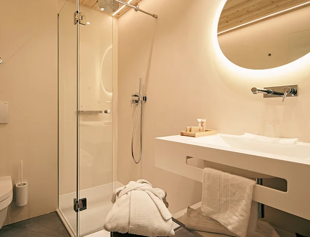 Helles Badezimmer im Einzelzimmer Zirbe mit Dusche, Waschbecken und beleuchtetem Spiegel