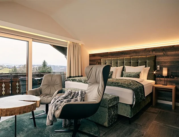 Doppelzimmer mit grünem Polsterbett, Sofa und Holztisch im modernen Alpenstil