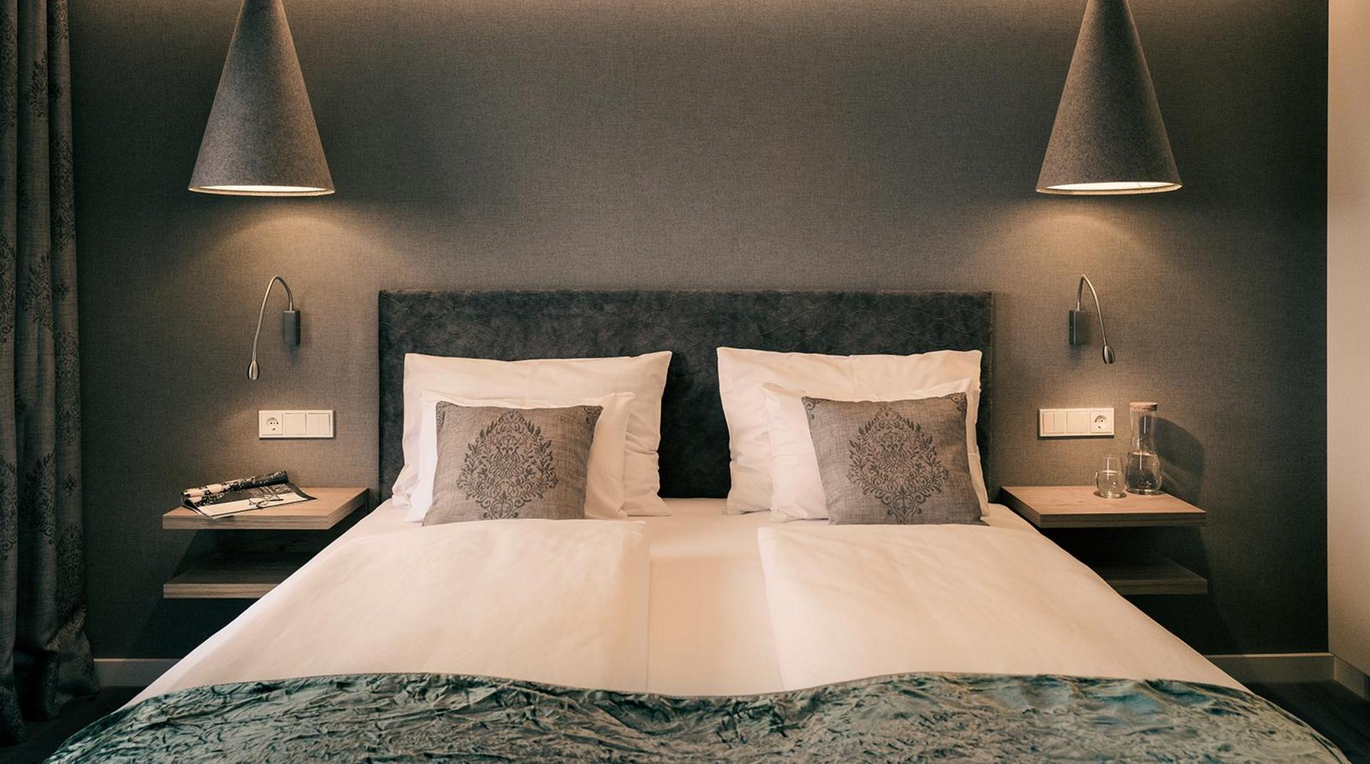 Modernes Doppelzimmer mit grauer Wand, Hängeleuchten und grünem Plaid.