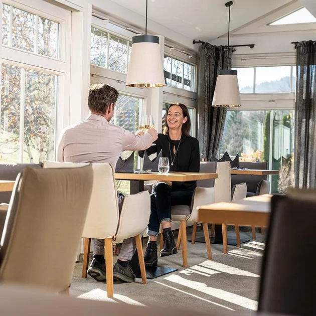 Zwei Gäste stoßen mit Wein im Wintergarten des Hotels an