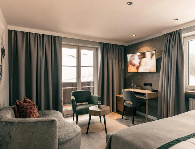 Modernes Doppelzimmer mit Schreibtisch, Sitzbereich und Balkon.