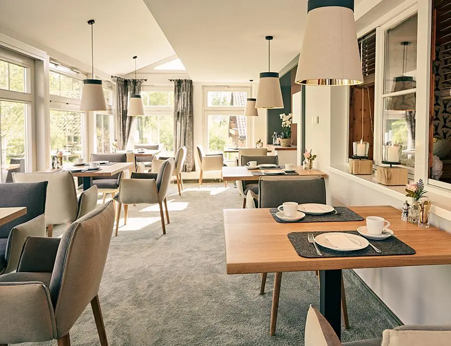 Heller Frühstücksraum mit großen Fenstern, gedeckten Tischen und modernen Lampen im Wintergarten des Hotel Birkenhof.