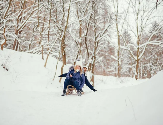 Vater rodelt mit Kind im Schnee beim Hotel Birkenhof in Oberstaufen