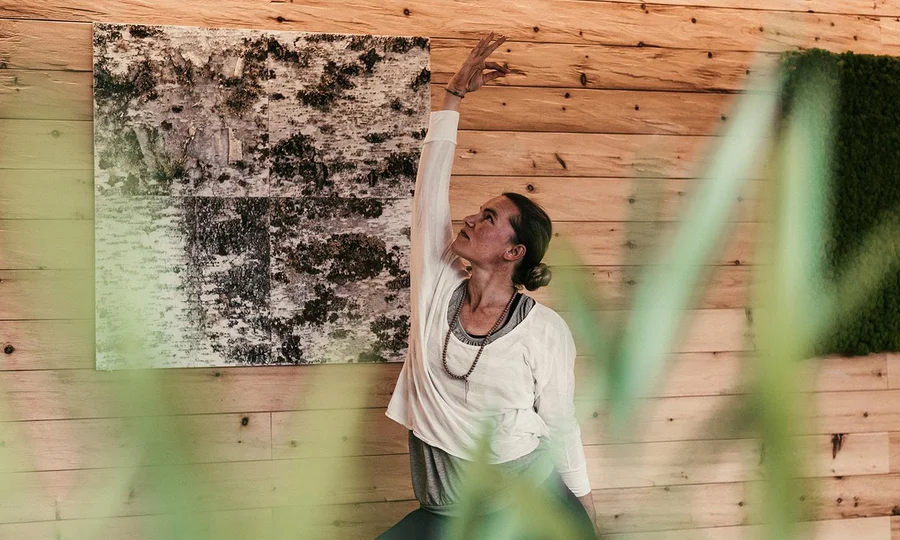 Schrothwoche_Yogastunde_Hotel_BirkenhoFrau macht Yoga-Dehnübung im Holzraum mit Naturmotiven an der Wand.f_Oberstaufen_Allgaeu
