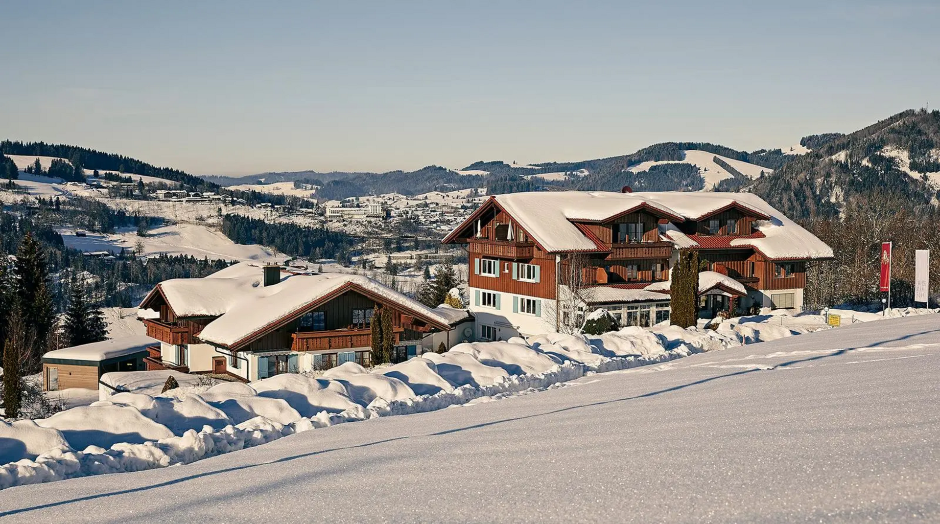 Außenansicht des Hotel Birkenhof in Oberstaufen im Winter, verschneite Dächer und umliegende Allgäuer Berglandschaft.