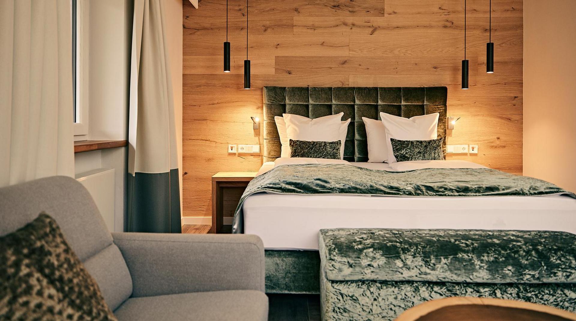 Modernes Doppelzimmer im Birkenhof Oberstaufen mit Samt-Kopfteil, Holzverkleidung und Sitzbereich.