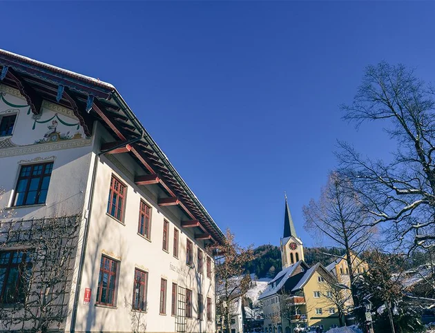 Ansicht auf Kirche und Gebäude im Ortskern von Oberstaufen bei blauem Himmel