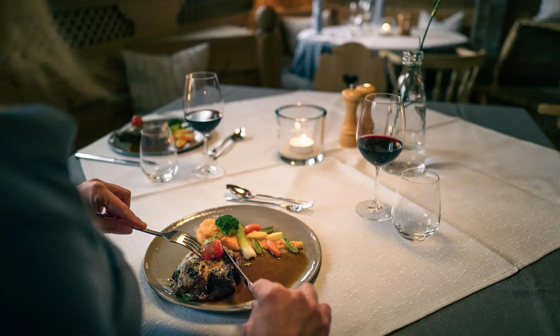 Gedeckter Restauranttisch mit Gourmetgericht, Rotwein und stimmungsvollem Kerzenlicht