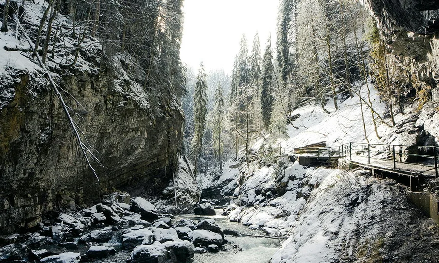 Flusslauf durch verschneite Felsen mit Holzsteg am Rand.