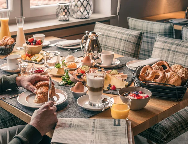 Reich gedeckter Frühstückstisch mit Brötchen, Aufschnitt, Obst und Kaffee.