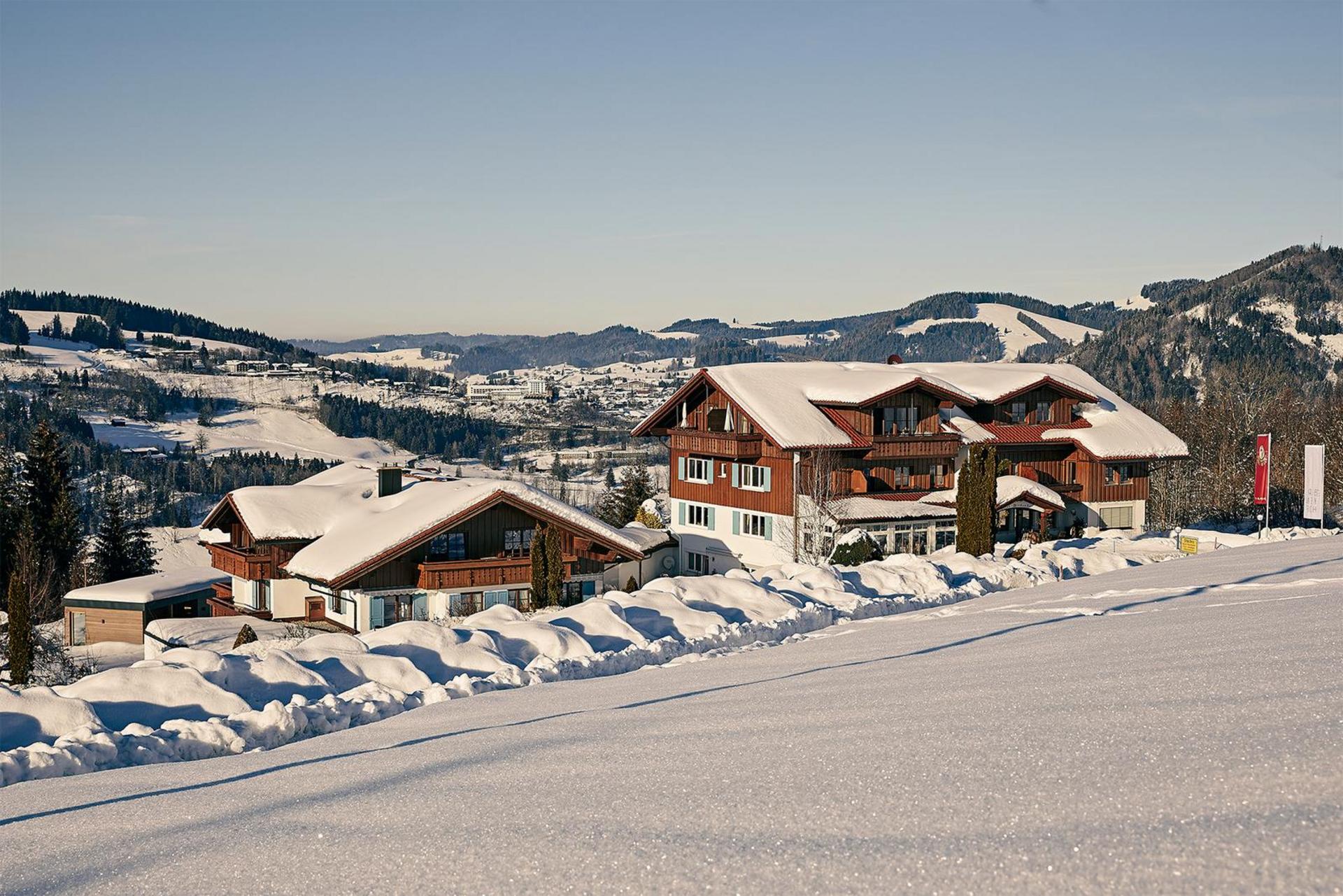 Winter_Hotel_Birkenhof_Oberstaufen_Allgaeu Panoramablick auf das Hotelensemble mit mehreren Alpenhäusern und verschneiter Berglandschaft im Hintergrund.