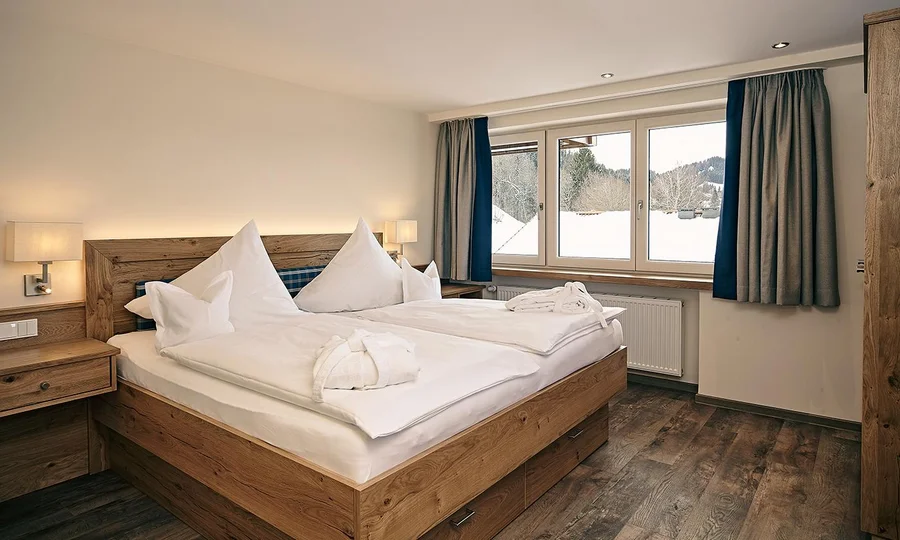 Helles Doppelzimmer mit Holzfußboden, großem Fenster und weiß bezogenem Doppelbett