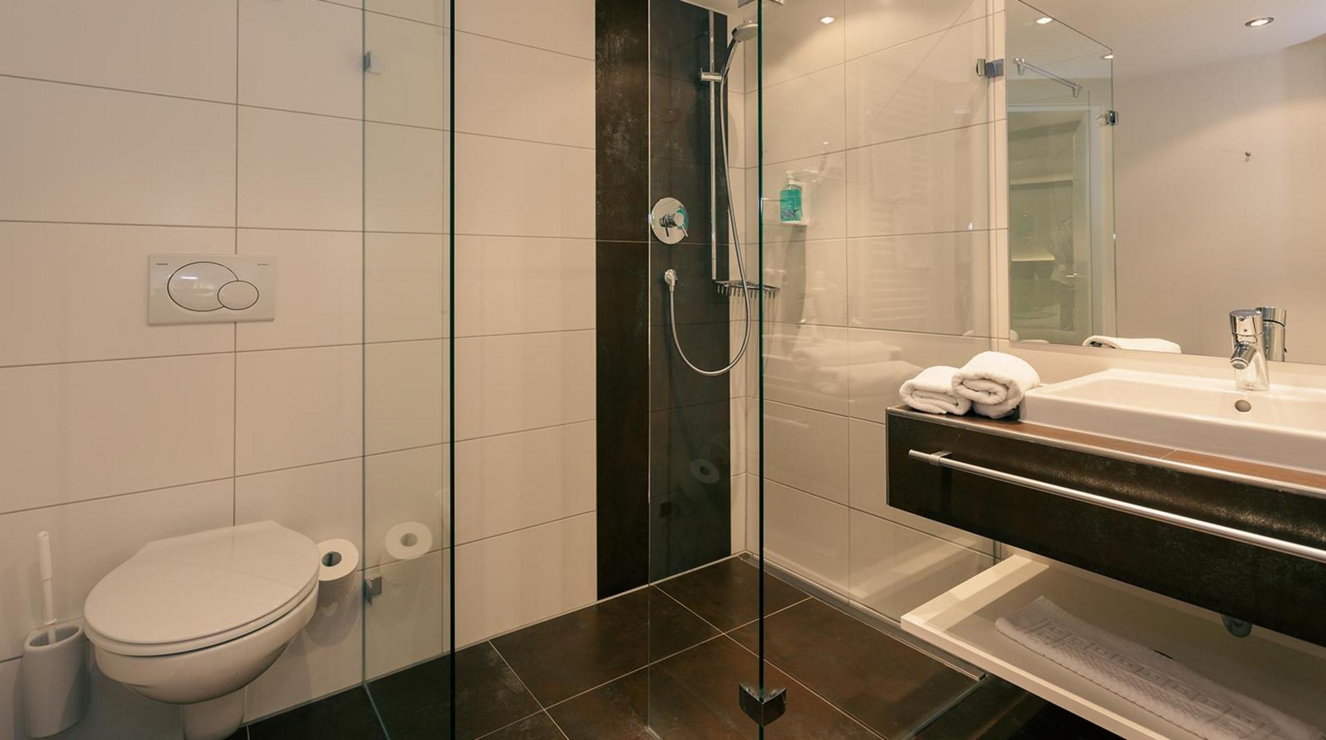 Modernes Bad mit bodengleicher Dusche, WC und großem Waschtisch.