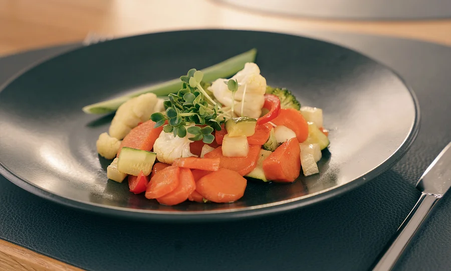 Gefüllte Zucchini mit Gemüse und Sprossen, dazu ein Glas Weißwein.