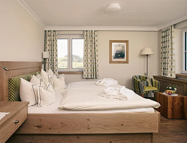 Helles Doppelzimmer mit zwei Fenstern, Holzbetten und gemütlicher Sitzecke.