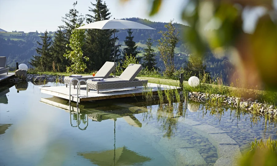 Naturbadeteich mit Holzplattform, Liegen und Sonnenschirm