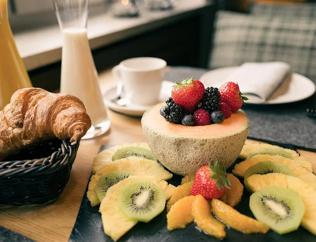 Teller mit aufgeschnittener Melone, frischen Beeren, Kiwi, Orange und Croissant.
