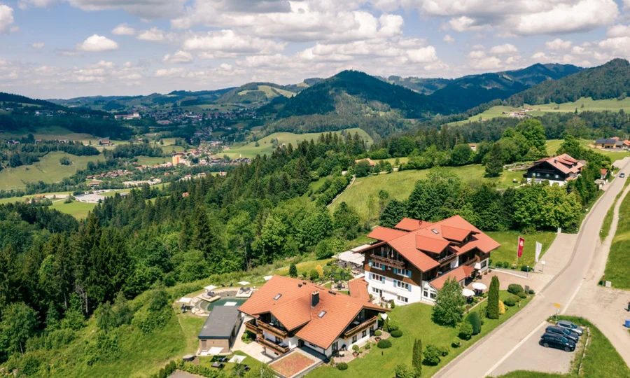 Sommeransicht der Hotelanlage mit Terrasse und Sonnenschirmen vor einer grünen Wiese