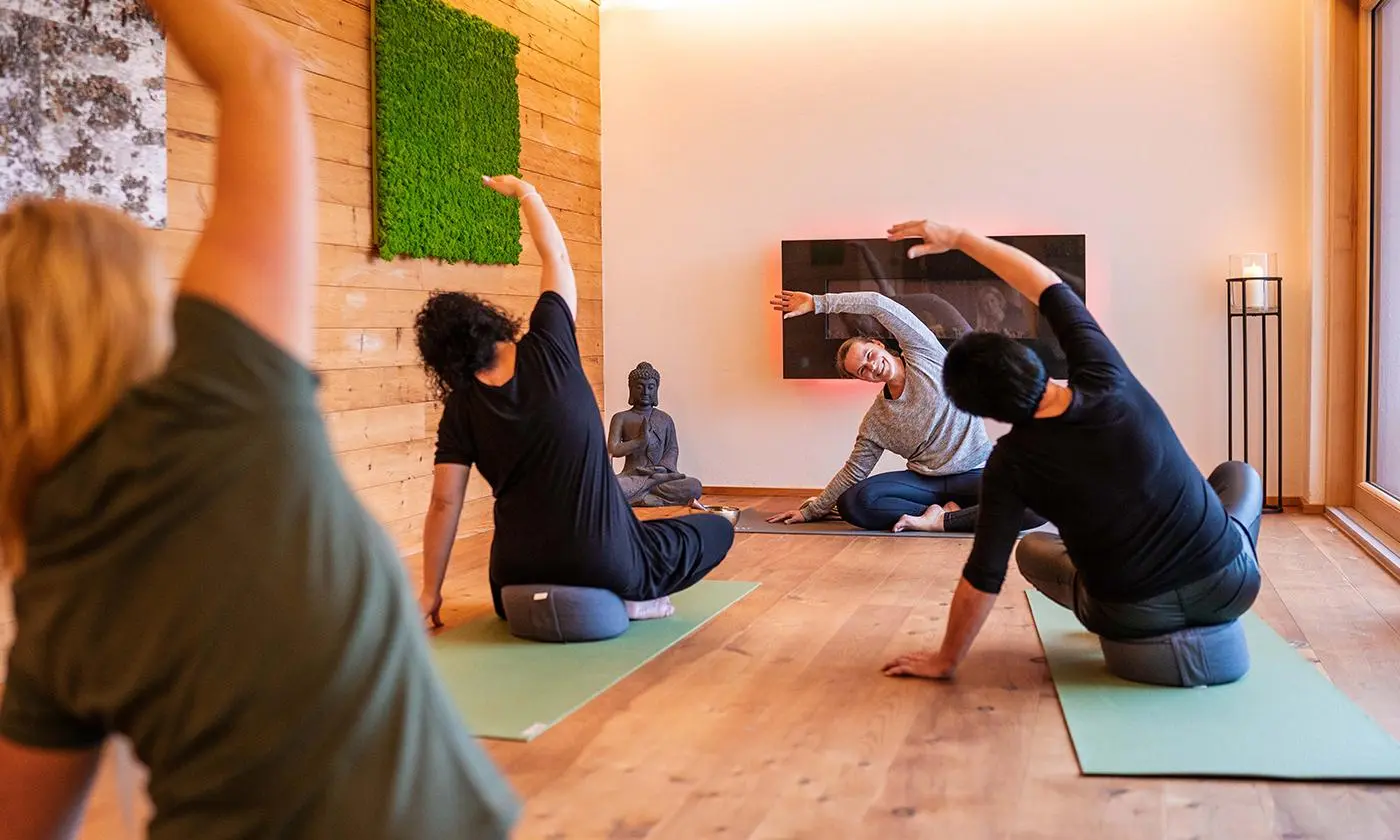 Yoga-Gruppe beim gemeinsamen Stretching auf Matten im NaturSpa-Bereich des Hotel Birkenhof mit entspannter Atmosphäre und Buddha-Statue