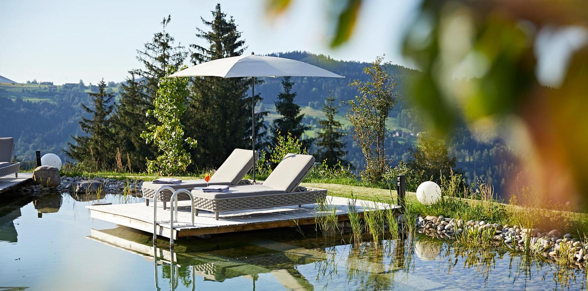 Sonnenterrasse am Natur-Schwimmteich des Hotels Birkenhof mit Liegen und Sonnenschirm.