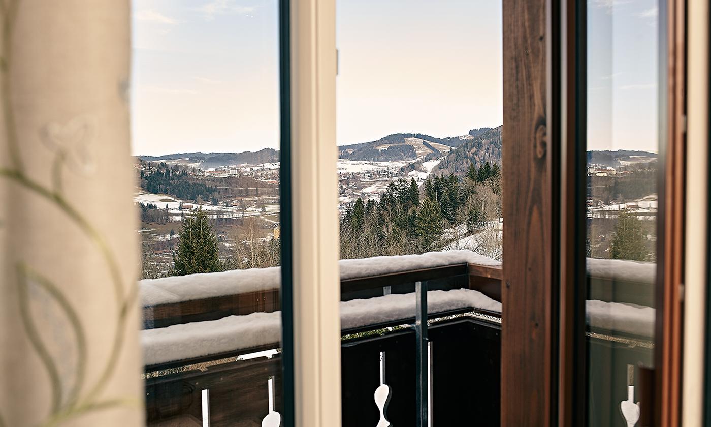 Blick vom Hotelzimmerbalkon auf verschneite Hügel, Wälder und eine winterliche Landschaft